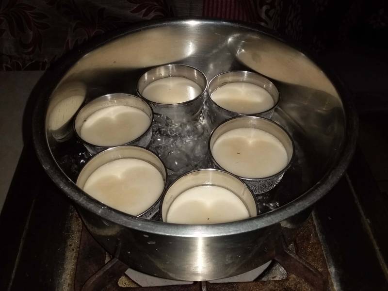 Steamed rice cake being prepared in boiling water in a container placed on oven.